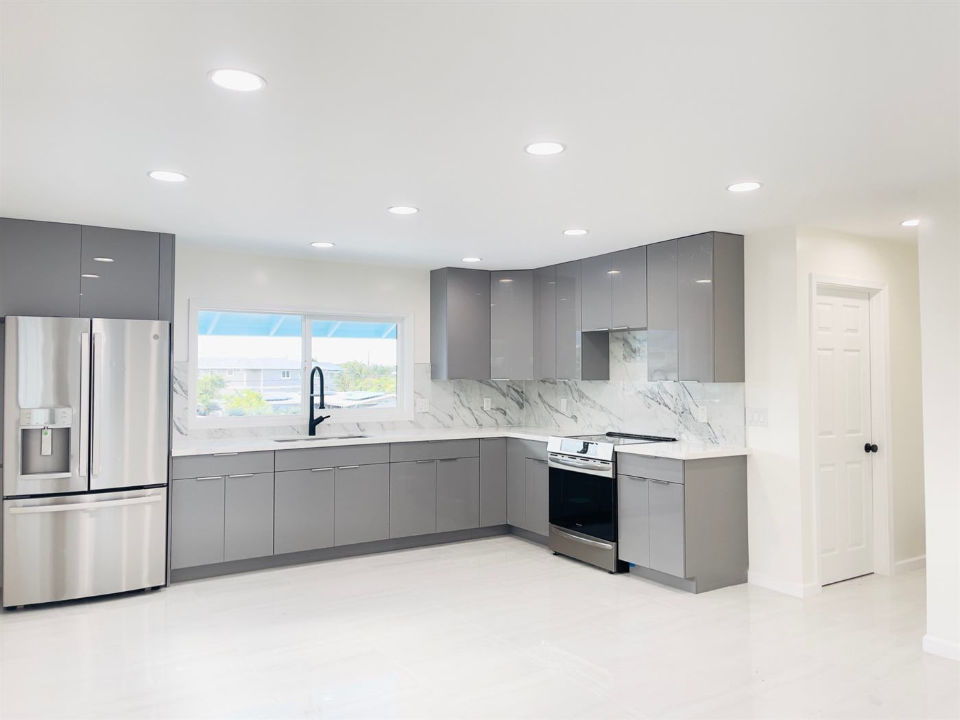 Remodeled kitchen with gray gloss cabinets and marble-look backsplash